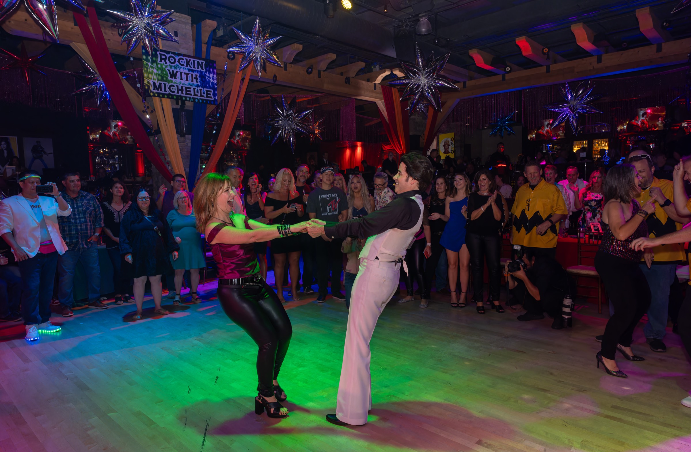 Smiling VIP guest dancing on the floor while a crowd watches a Travolta-inspired performance.